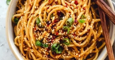 Bowl of easy garlic sesame noodles garnished with green onions and sesame seeds