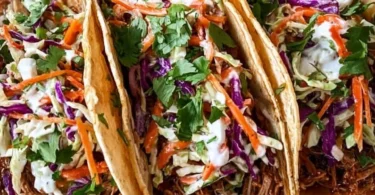 Delicious pulled pork tacos topped with tangy slaw on a rustic wooden table.