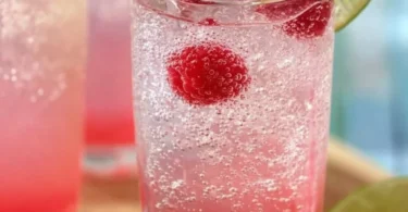A glass of Raspberry Key Lime Soda filled with ice and garnished with lime slices.